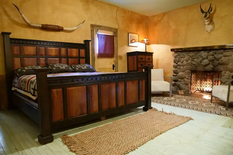 A king room with a carved wooden bed, a stone fireplace and an armchair
